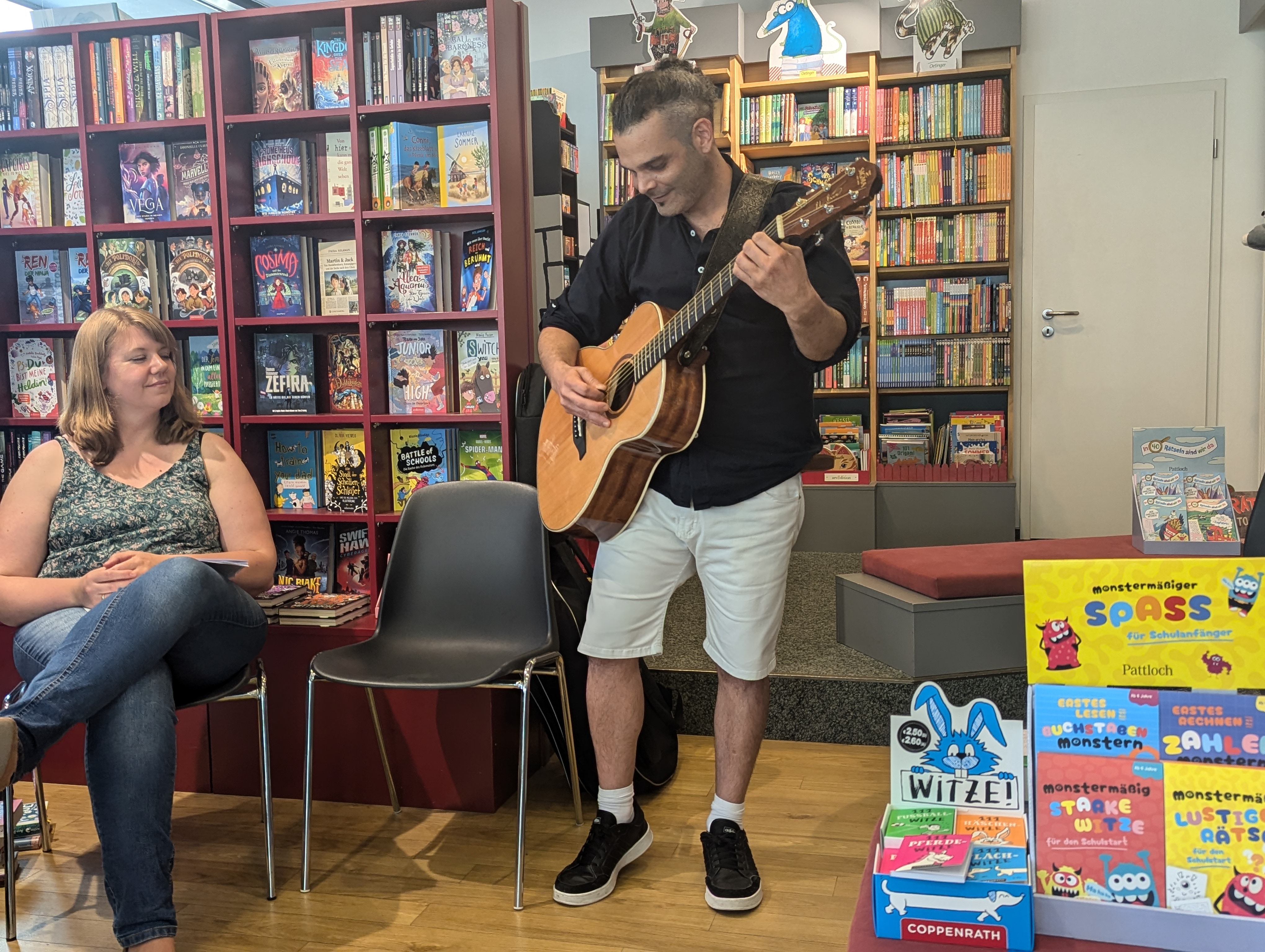 Mann stehend mit Gitarre Frau sitzend auf Stuhl